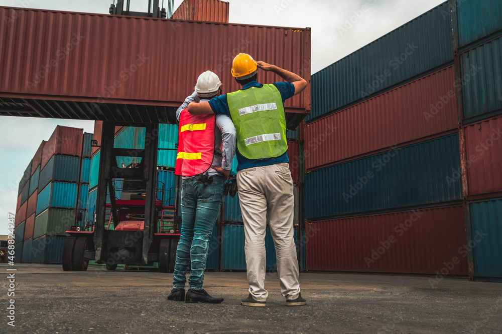 Industrial worker works with co-worker at overseas shipping container yard . Logistics supply chain 