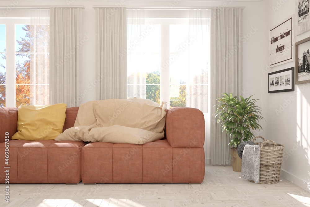 Stylish room in white color with sofa and autumn landscape in window. Scandinavian interior design. 