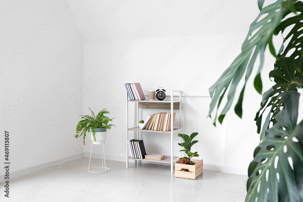 Wooden bookcase with alarm clock and houseplants near light wall