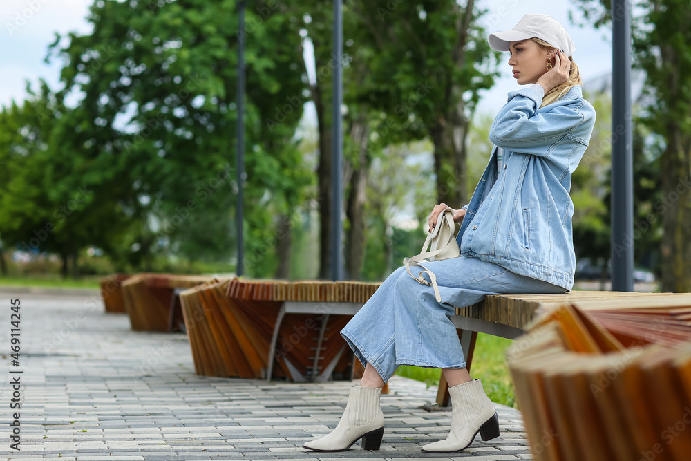 戴棒球帽的时髦女人坐在户外长椅上