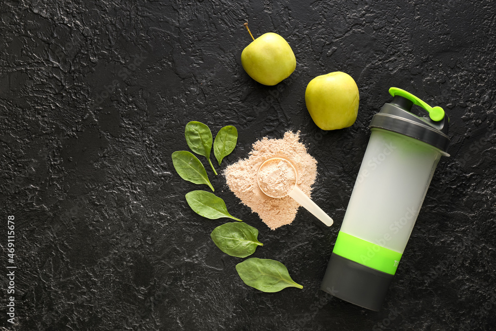 Measuring scoop with powder, bottle with protein shake, spinach leaves and apples on dark background