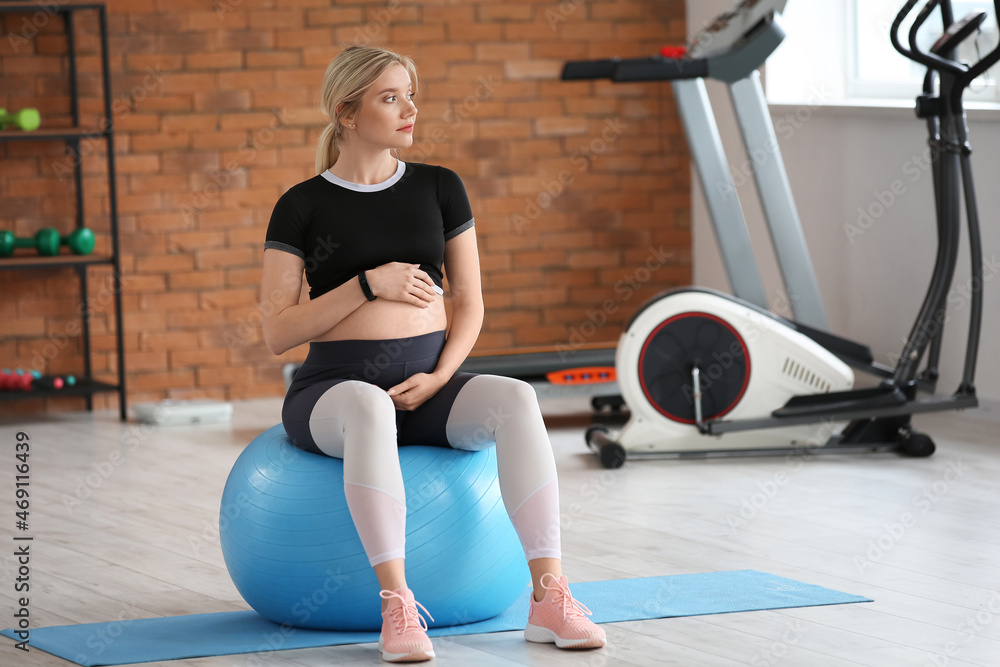 Young pregnant woman training with fitball in gym