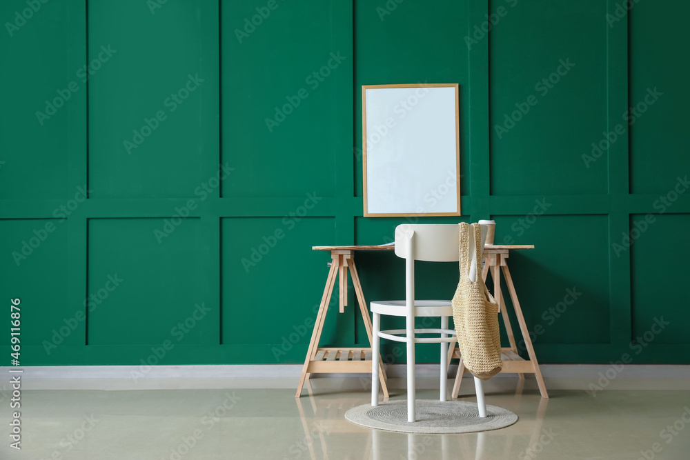 Modern workplace with cup of coffee and blank frame hanging on green wall