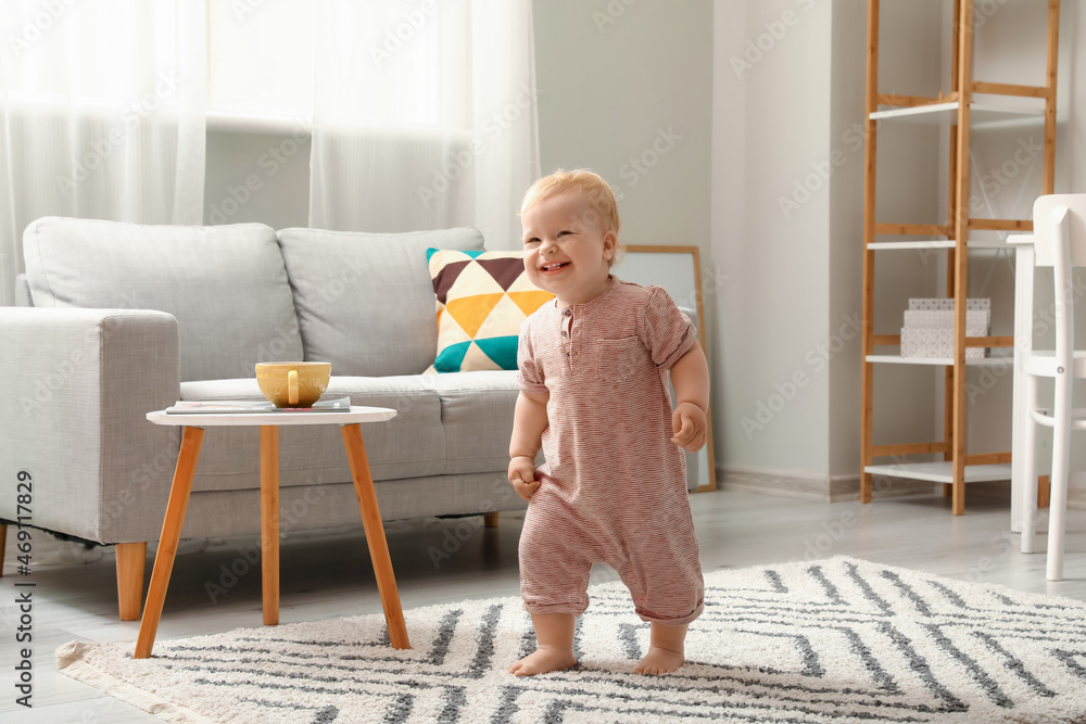 Cute baby girl in bodysuit learning to walk at home