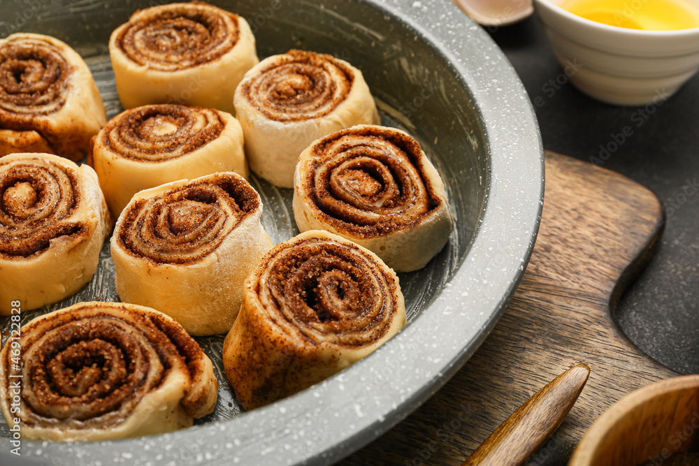 Baking dish of uncooked cinnamon rolls on black background, closeup