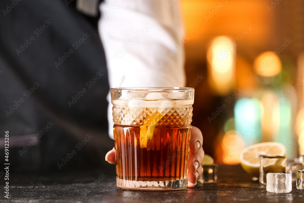 Female bartender with glass of tasty Cuba Libre cocktail on table in bar