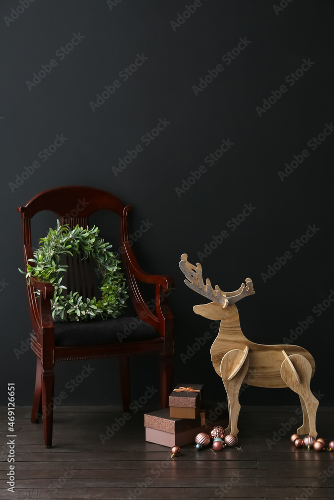 Wooden reindeer, armchair, Christmas wreath and gift boxes near dark wall