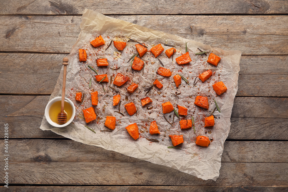 Parchment with tasty roasted pumpkin pieces on wooden background