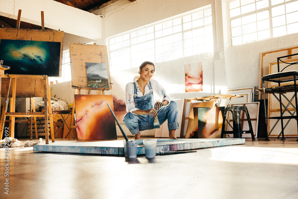 Cheerful young artist squatting close to her painting