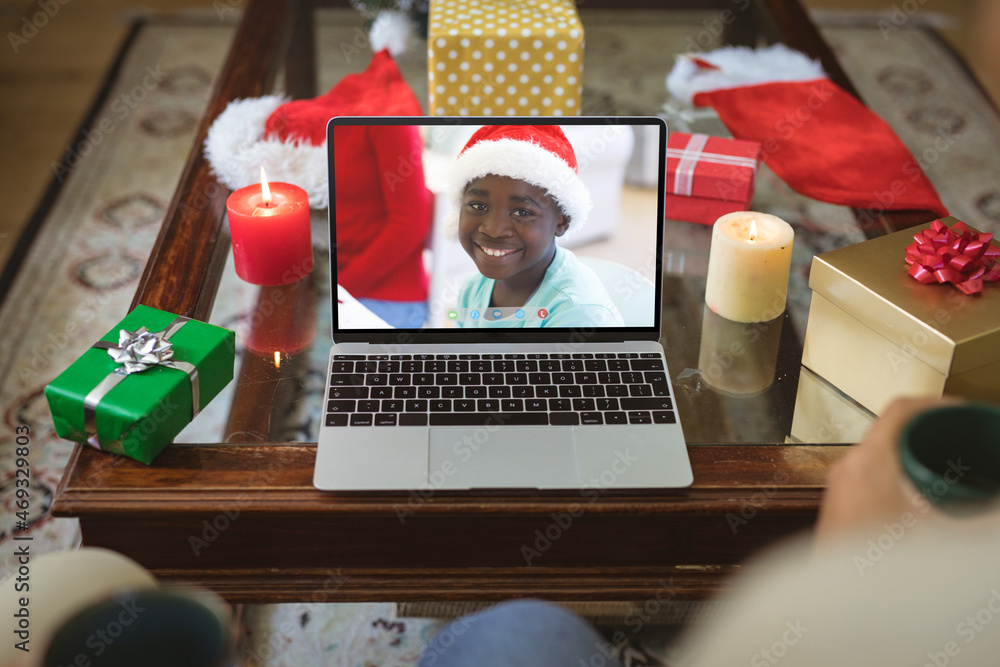 Happy african american boy in santa hat smiling on laptop video call screen at christmas time