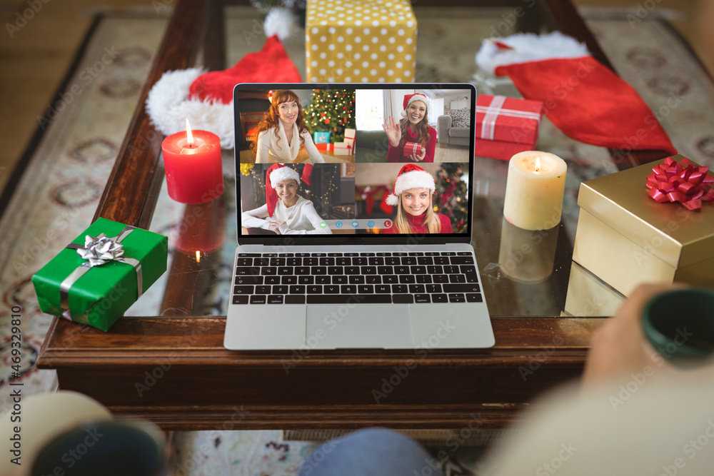 Smiling caucasian female friends in santa hats on laptop group video call screen at christmas