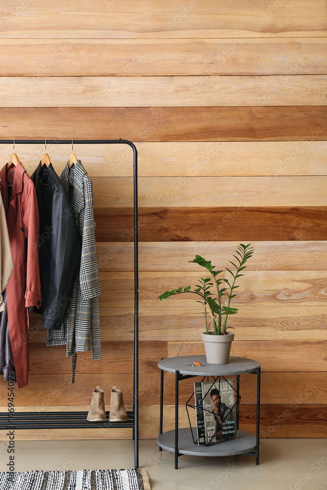 Rack with female outwear clothes, shoes and table near wooden wall