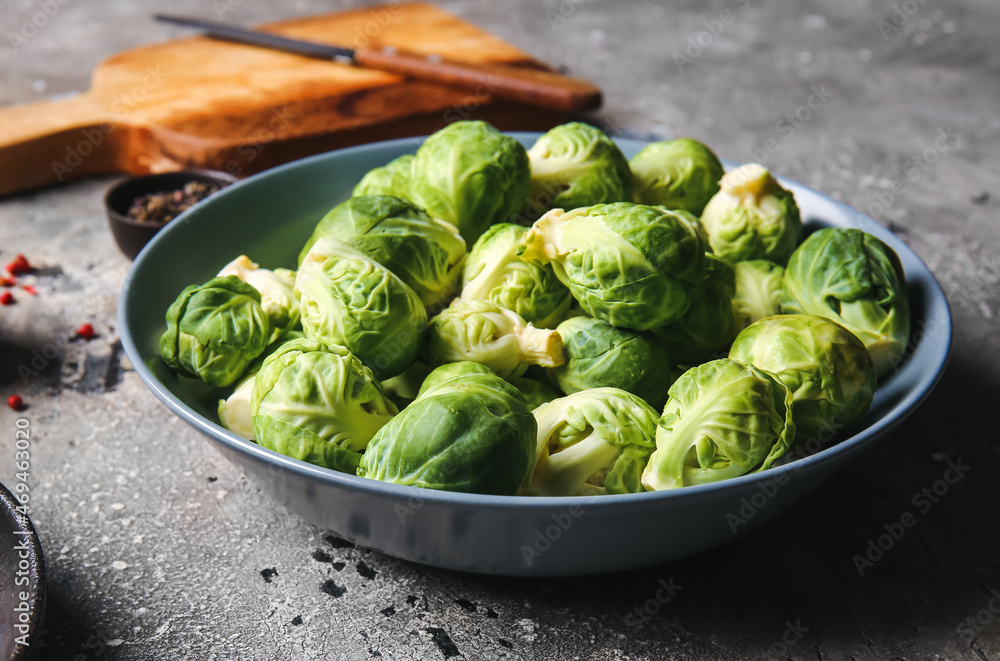 Bowl with raw Brussels cabbage on grey background