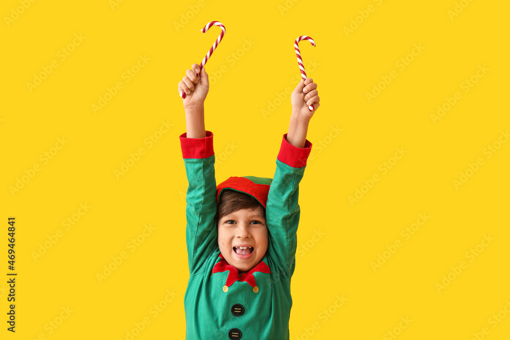 Cute little elf with candy canes on color background