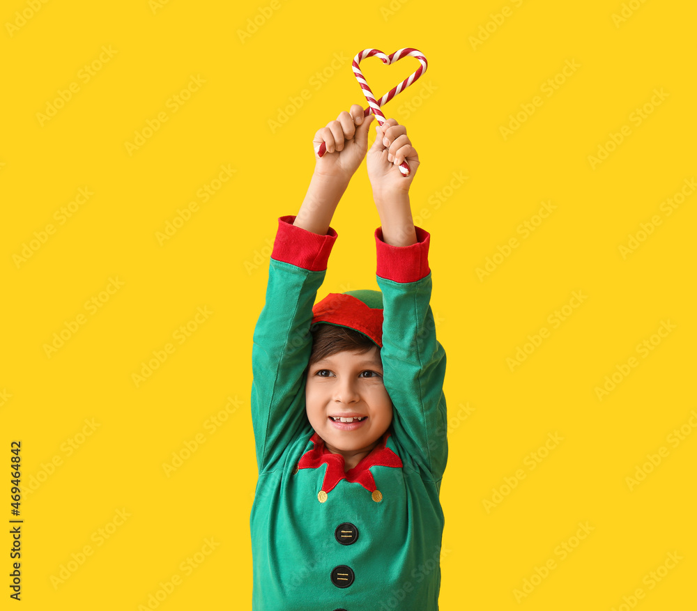 Cute little elf with candy canes on color background