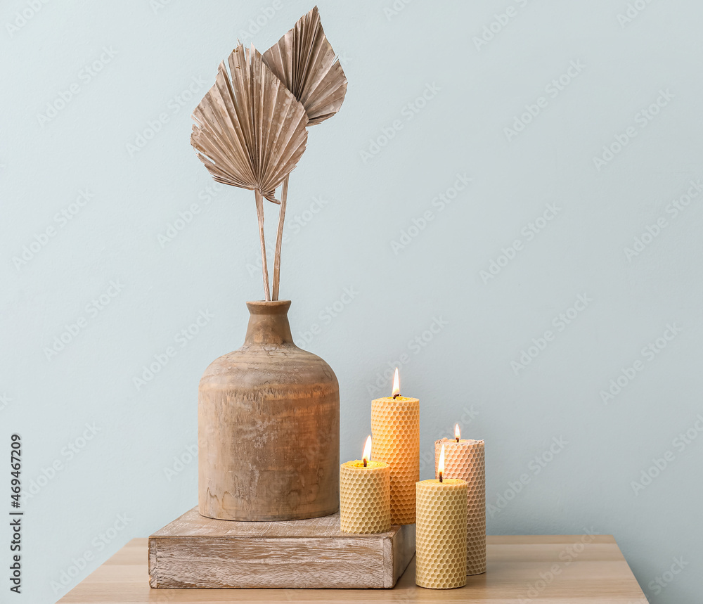 Burning candles and vase with decor on table near color wall