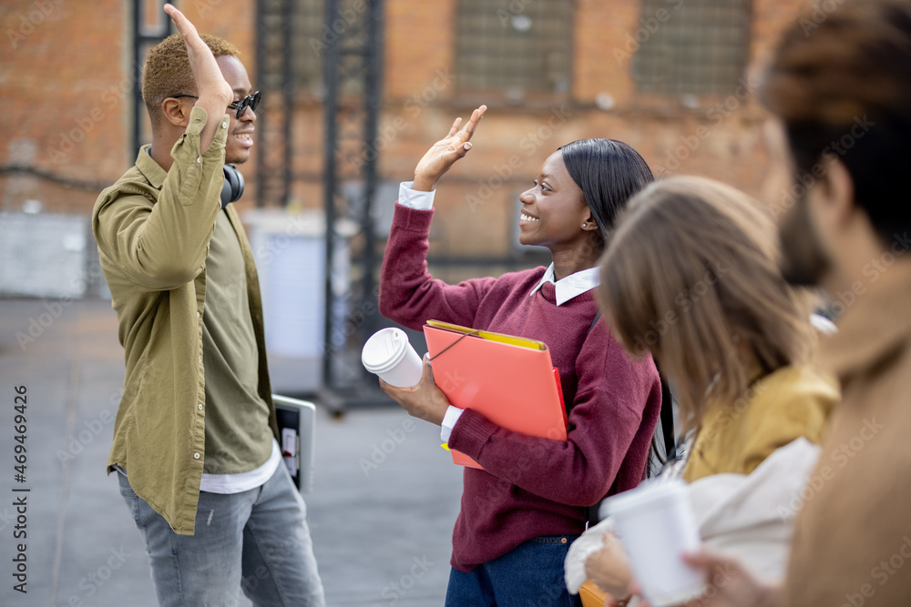 Black girl and guy holding hands of each other near their multiracial friends. Concept of education 