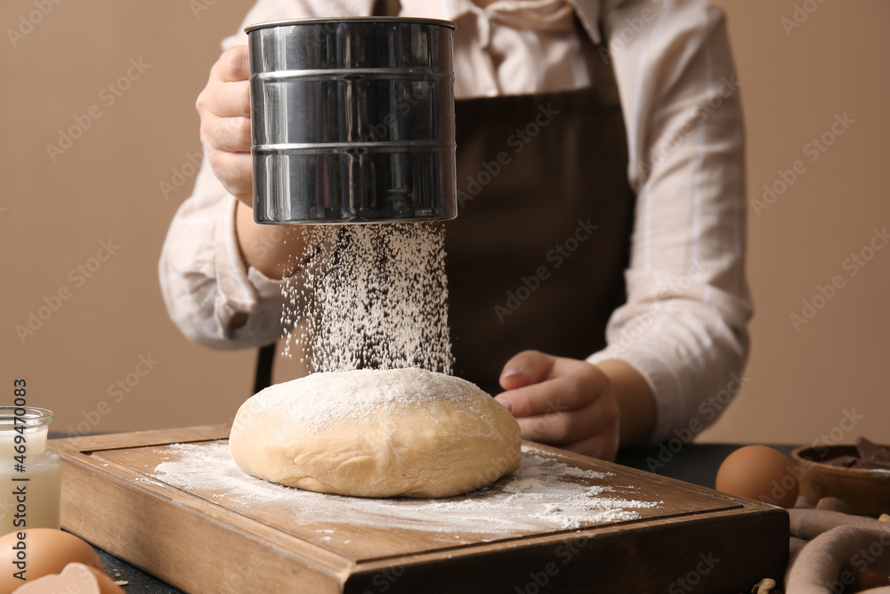 Woman adding flour onto dough for preparing homemade cookies at kitchen table