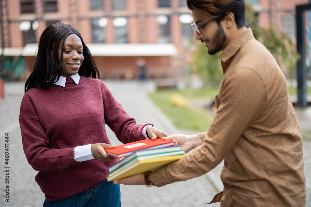 Indian man giving books to black girl outdoors. Concept of education and learning. Idea of students 