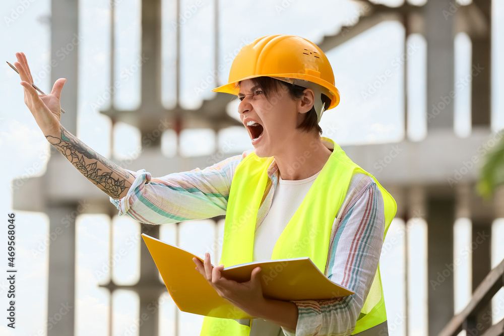 Angry female construction worker in hardhat with folder outdoors