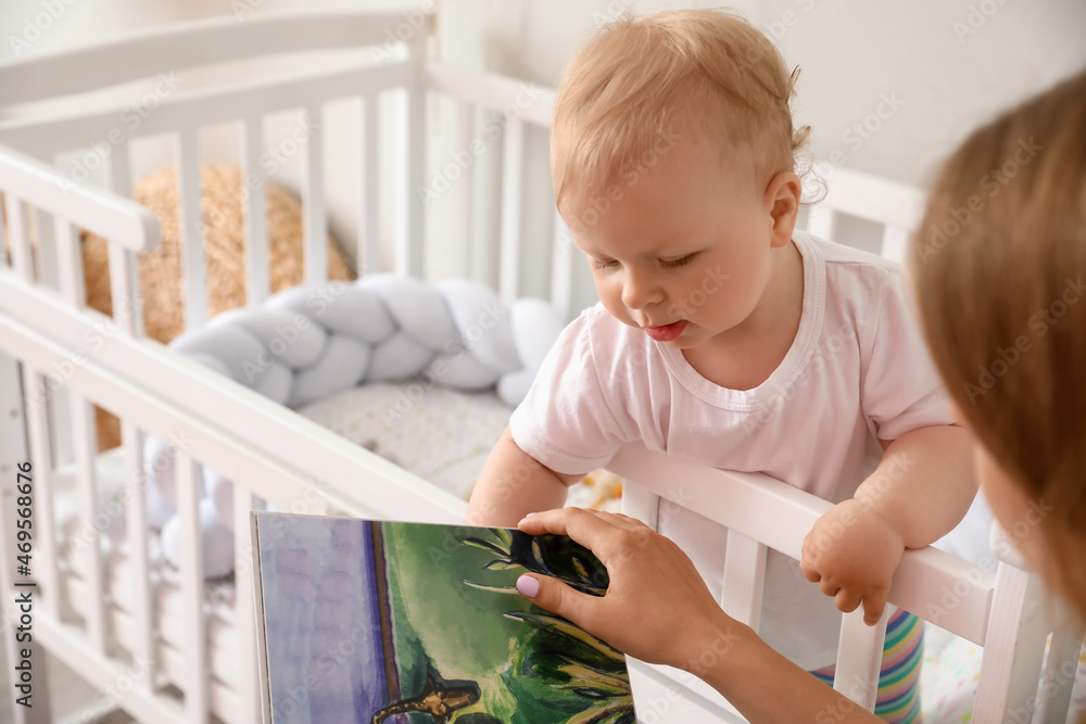 Mother reading book to her cute little baby in crib