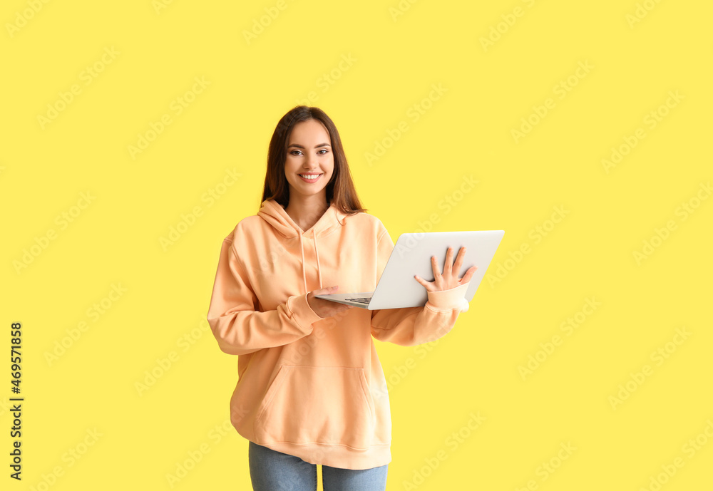 Beautiful young woman in stylish hoodie and with laptop on color background