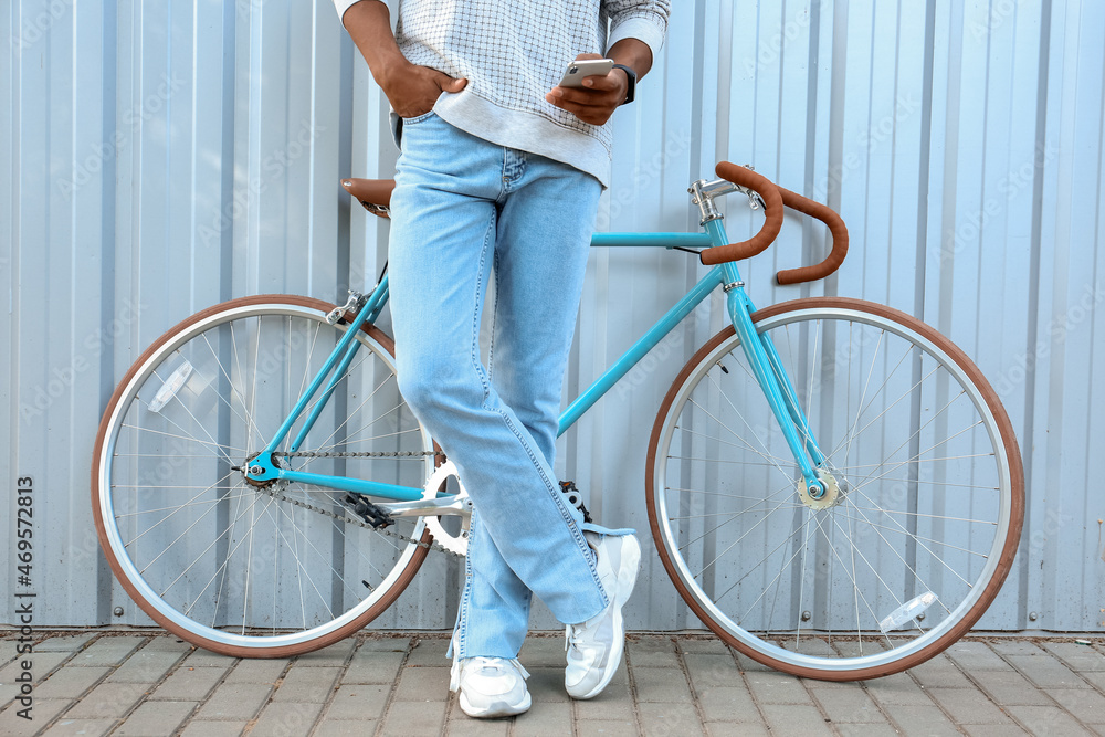 African-American teenage boy with bike using mobile phone near blue fence