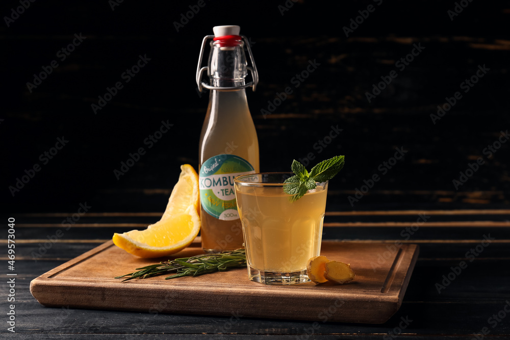 Bottle and glass of tasty kombucha on dark wooden background