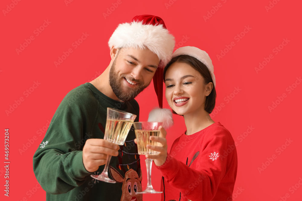 Young couple in stylish Christmas clothes and with glasses of champagne on color background