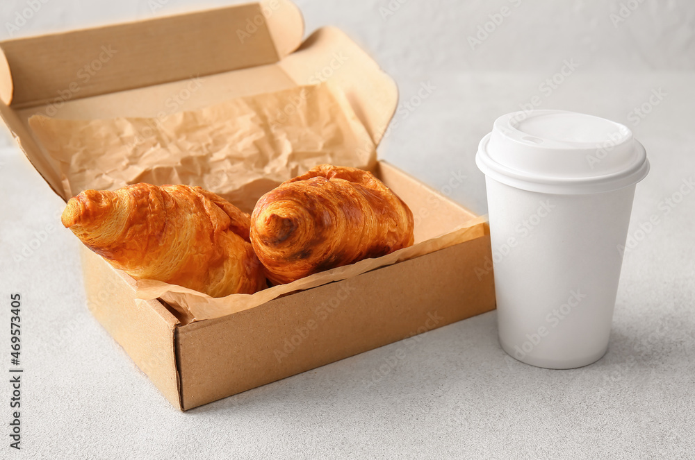 Box with delicious croissants and cup of beverage on white background