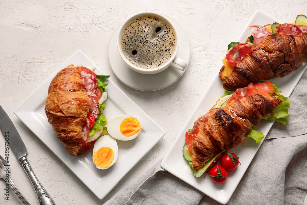 Plates with delicious croissant sandwiches and cup of coffee on white background