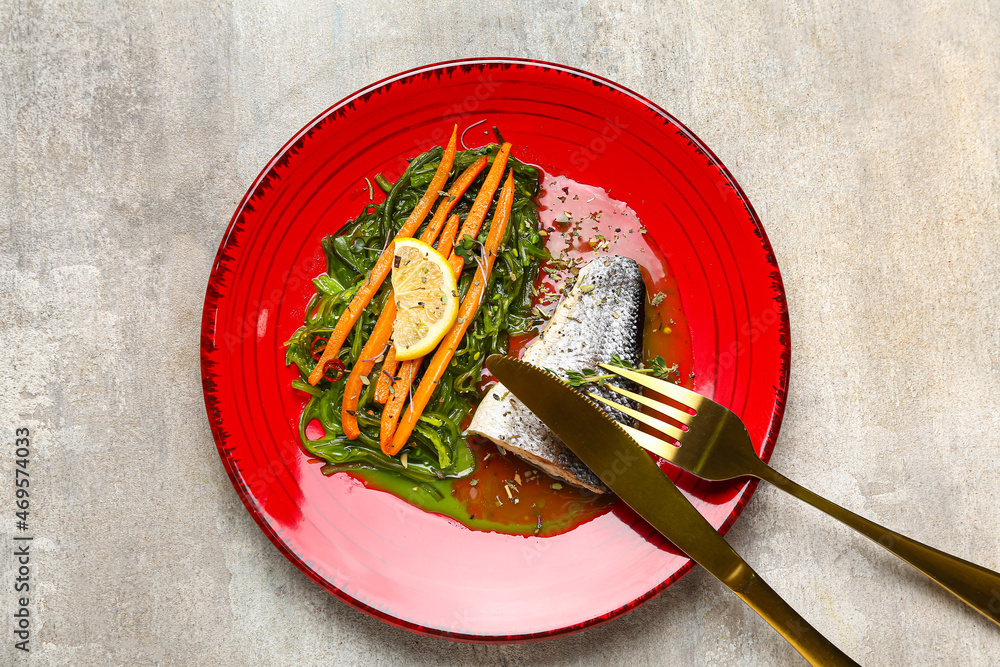 Plate of tasty sea bass fish with vegetables on grey background