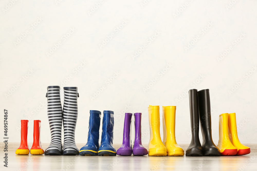 Many different rubber boots on floor near light wall