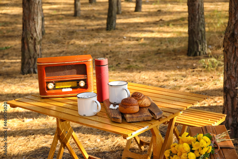 Tasty buns with hot chocolate and radio receiver on table in autumn forest