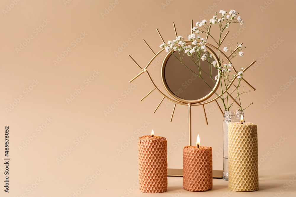 Burning candles, mirror and gypsophila flowers on beige background