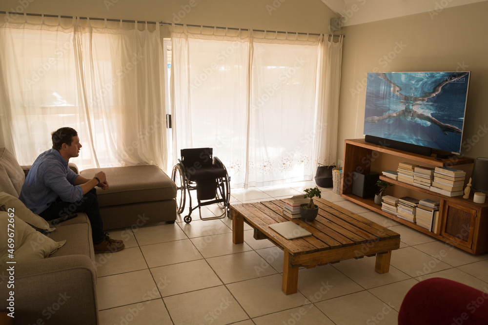 Caucasian disabled man sitting at home watching swimming competition on tv