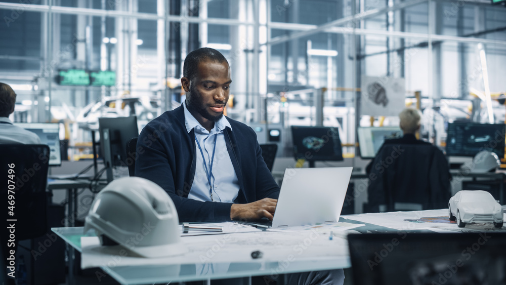 Young African American Engineer Working on Laptop Computer in an Office at Car Assembly Plant. Indus