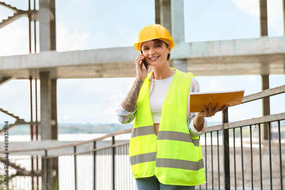 Female construction worker with folder talking by mobile phone outdoors