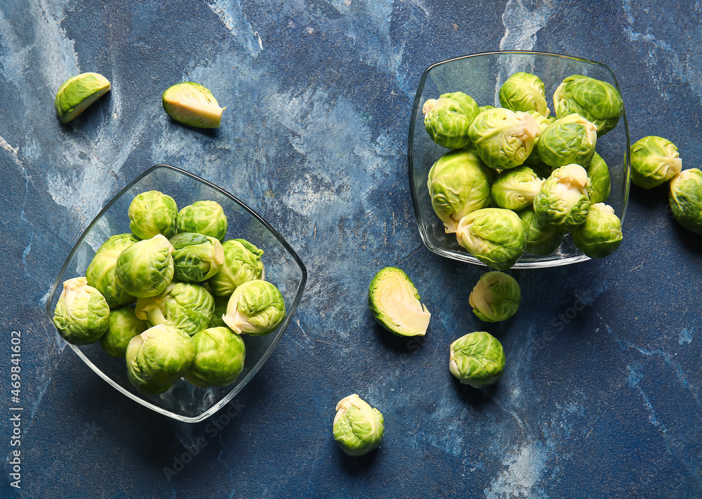 Bowls with fresh raw Brussels cabbage on blue background