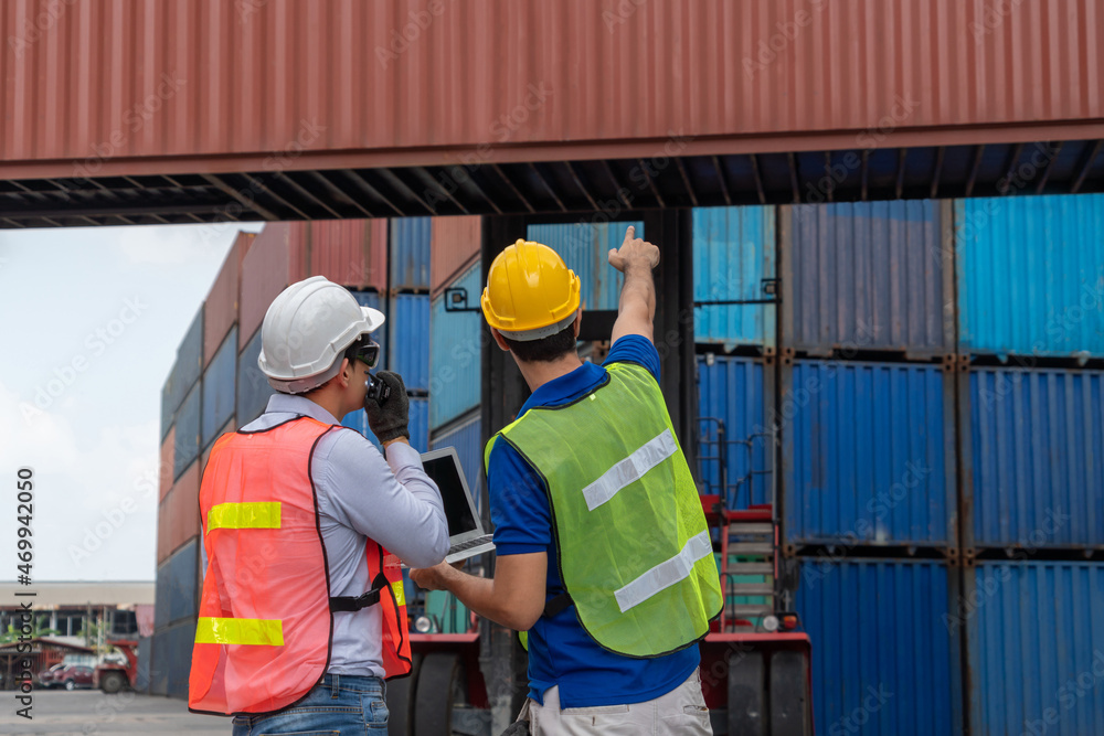 Industrial worker works with co-worker at overseas shipping container yard . Logistics supply chain 