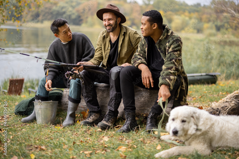 Multiracial male friends resting and talking in nature. Men after fishing on river or lake coast. Co