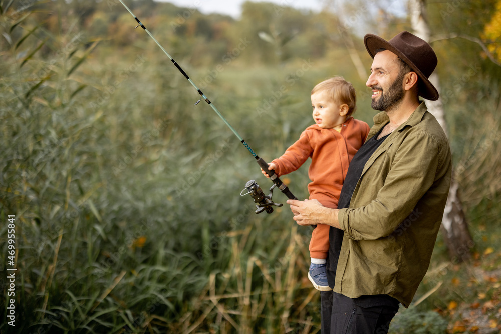 Smiling caucasian man fishing with little son on river or lake coast. Concept of leisure and weekend