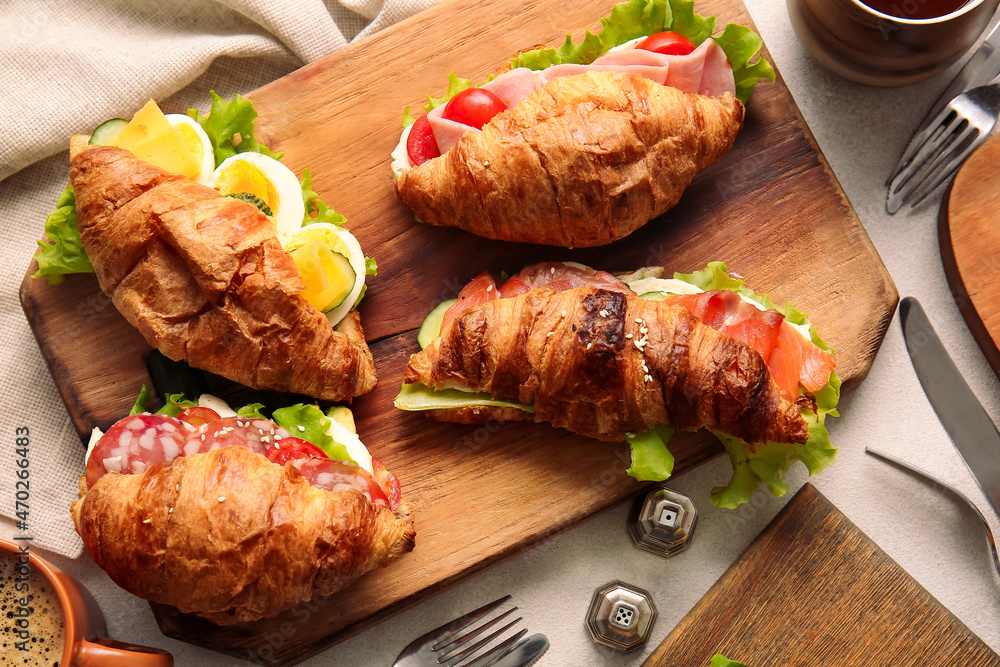 Wooden board with delicious croissant sandwiches on white background