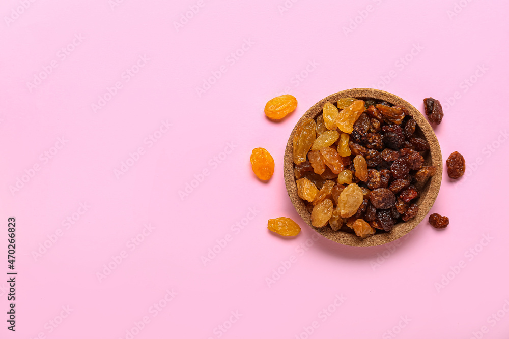 Bowl with tasty raisins on pink background