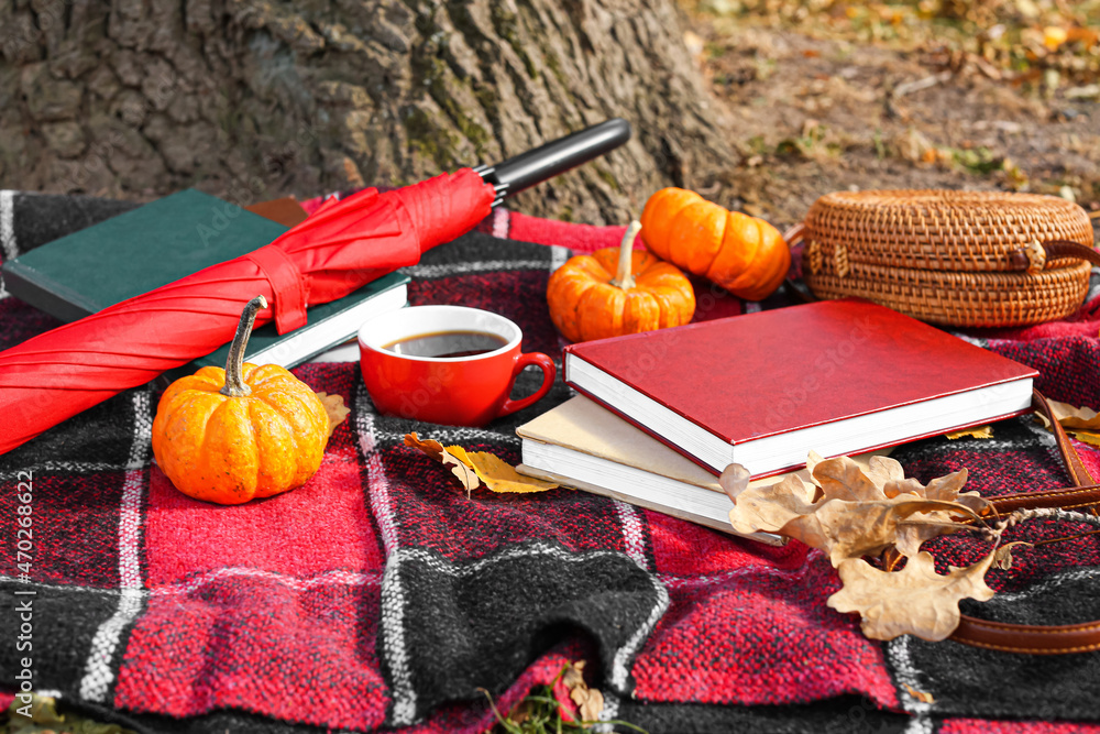 Stack of books, cup of coffee, umbrella, female bag, pumpkins and autumn leaves on plaid in park