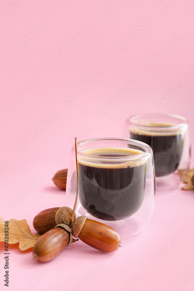 Glass cups of coffee with acorns on pink background