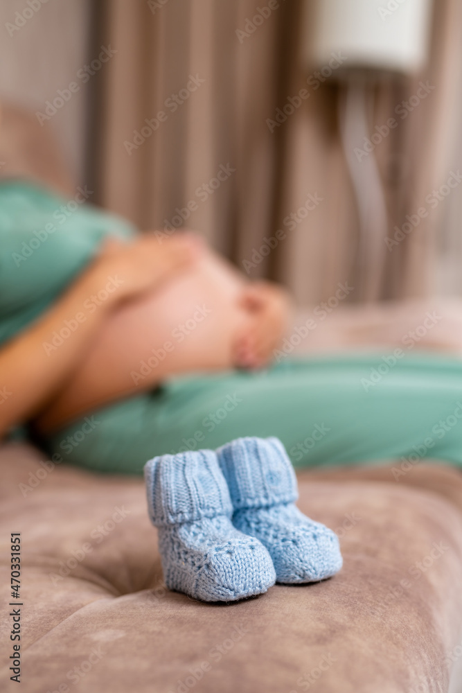 Tiny blue knitted baby booties for future newborn boy. Little baby socks on the couch. Blurred image