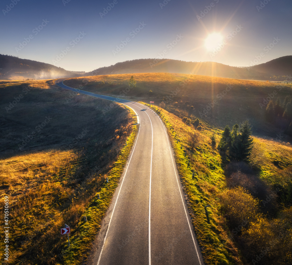 Aerial view of mountain road in forest at sunset in autumn. Top view from drone of road in woods. Be