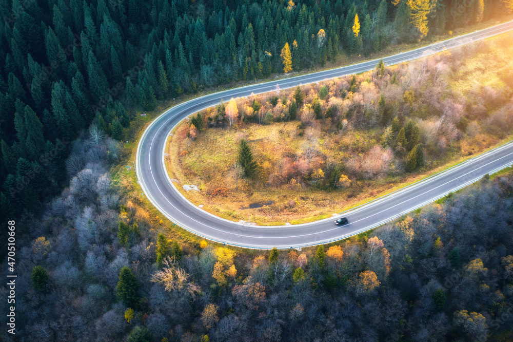 Aerial view of mountain road in forest at sunset in autumn. Top view from drone of road in woods. Be