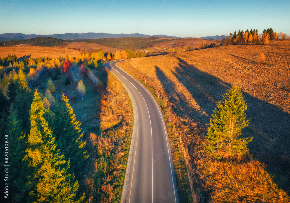 Aerial view of mountain road in forest at sunset in autumn. Top view from drone of road in woods. Be